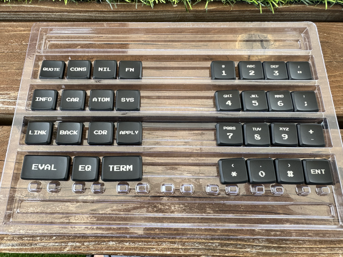 The KN-86 custom keycap set — black MBK caps with amber Press Start 2P legends: QUOTE, CONS, NIL, FN, CAR, CDR, and the phone-style numpad